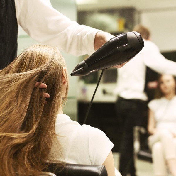 stylist drying girls hair with hair dryer in beauty salon